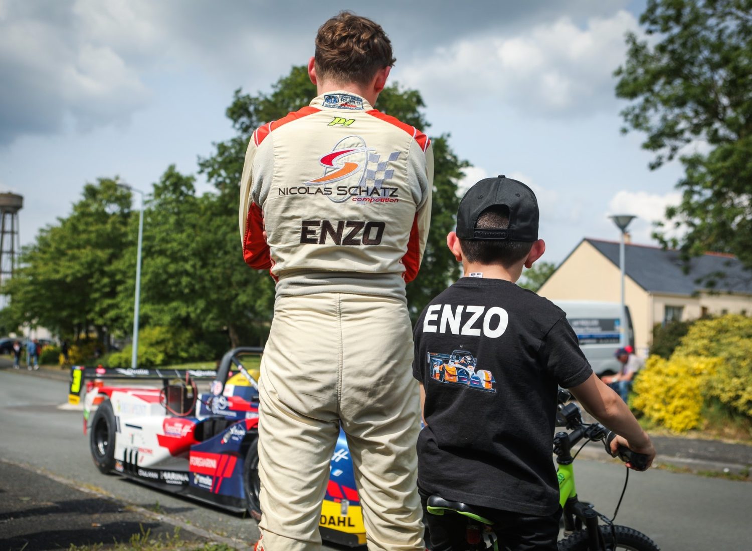 Un pilote de la Course de Côte et un enfant attendent que les billets arrivent devant des véhicules