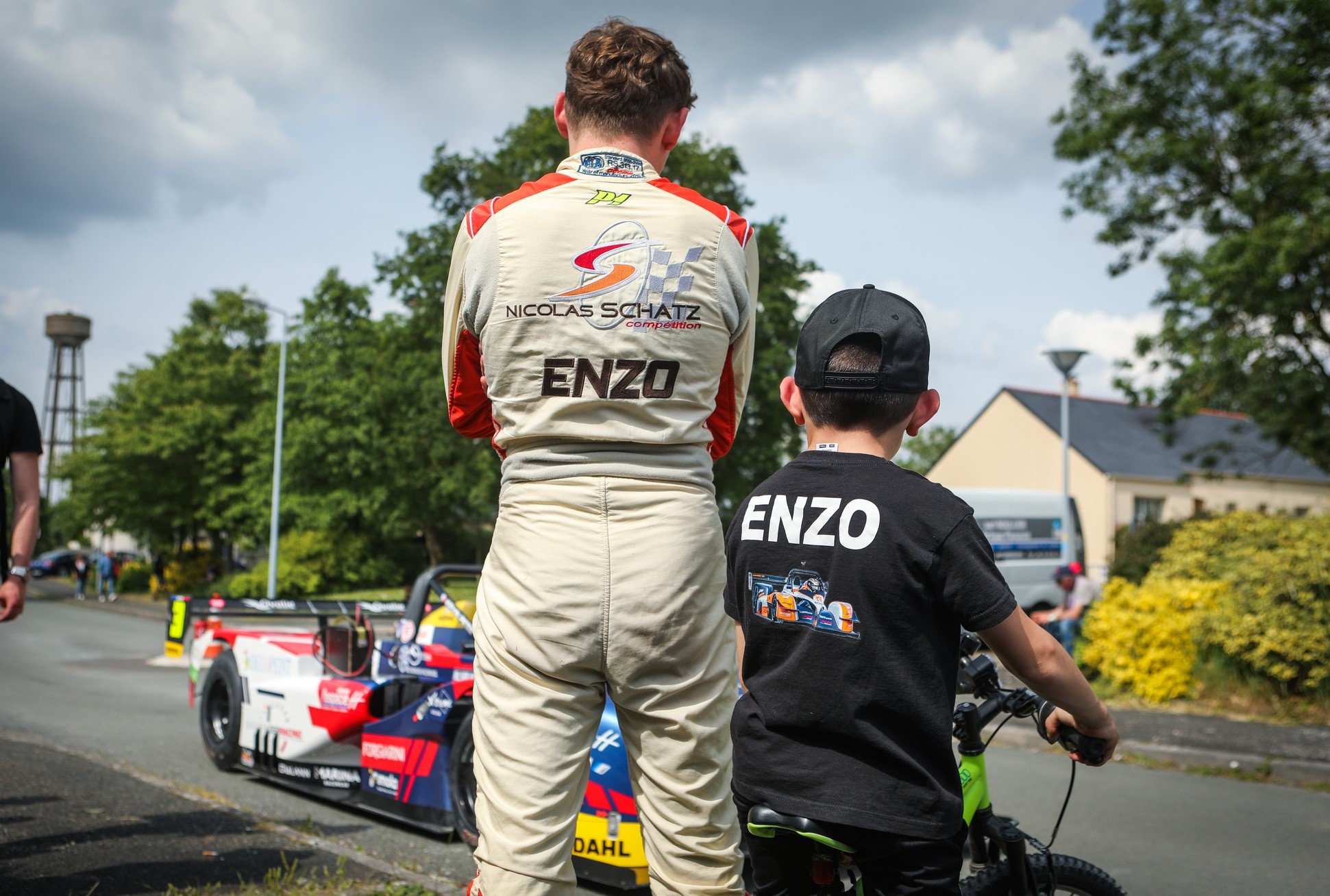 Un pilote de la Course de Côte et un enfant attendent que les billets arrivent devant des véhicules